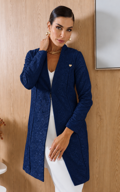 Vista frontal do jaleco feminino de alfaiataria azul-marinho, com tecido jacquard floral, gola estruturada e pequeno coração dourado.