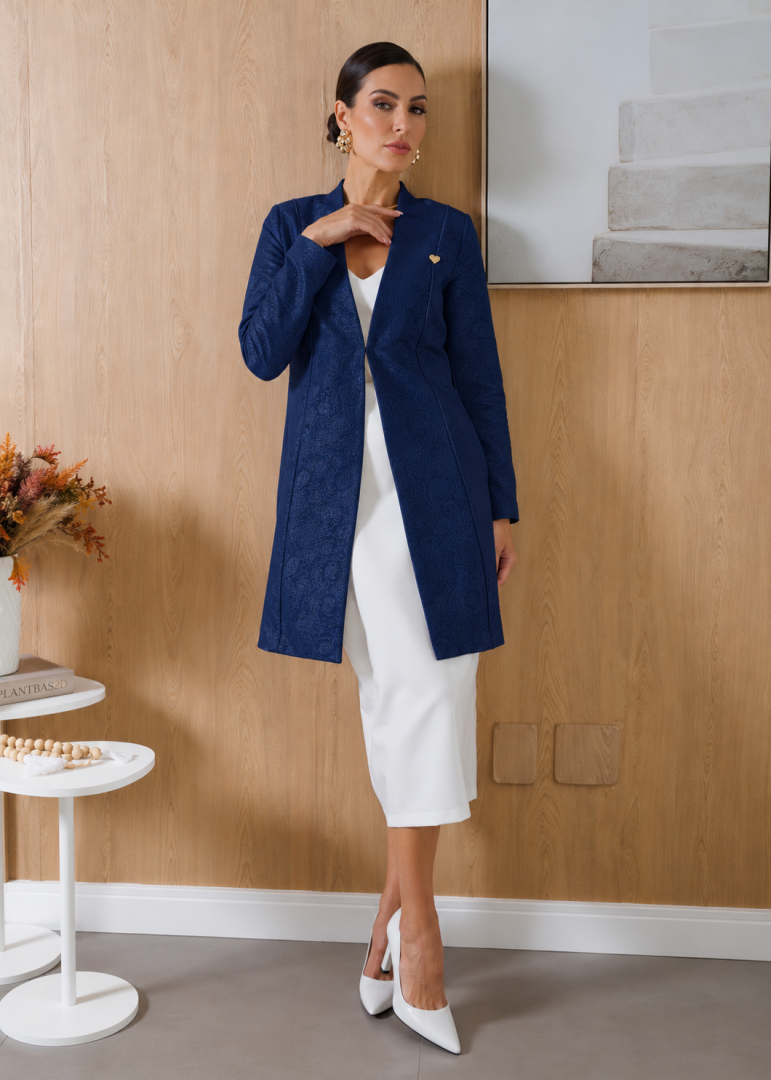 Modelo vestindo jaleco feminino estilo blazer azul-marinho em jacquard floral, com mangas longas, modelagem alongada e detalhe dourado.